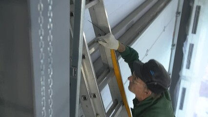Professional worker climbing up ladder indoors to repair a transformer. Man in a workwear