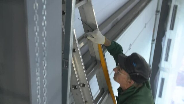 Professional worker climbing up ladder indoors to repair a transformer. Man in a workwear