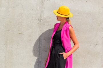 Fashionable girl on the background of a concrete wall, trendy style, pink jacket and yellow hat