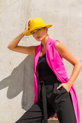 Fashionable girl on the background of a concrete wall, trendy style, pink jacket and yellow hat