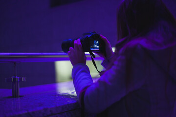 Woman taking pictures at night in the dark with purple neon light holding a dslr camera,...