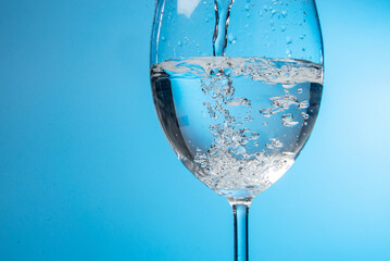 Pouring water into a glass against light blue background. fresh water a glass with bubbles blue background