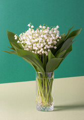 Bouquet of forest lilies of the valley in a vase on creative yellow-green background. Festive vertical card