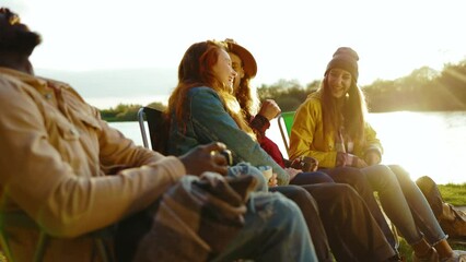 At sunlight hipster friends sitting near campfire in nature. Young people talk plays with dog smiling feel happy. Vacation tourism adventure outdoors. Slow motion