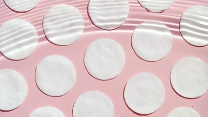 Radial water ripples over pale pink background with cotton pads arranged in rows | Background shot for facial toner commercial