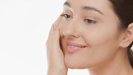 Big close-up of beautiful Caucasian woman strokes her cheek smiling on white background | Skin moisturizing concept