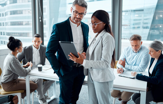 Be smart about your business processes. Shot of two businesspeople using a digital tablet in an office with their colleagues in the background. - Powered by Adobe