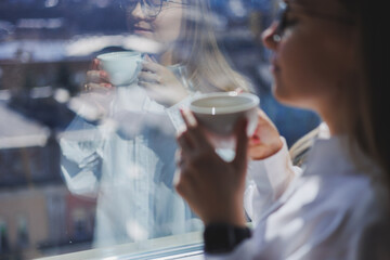 A woman in a white shirt with fragrant hot coffee in her hands. Close-up woman's hands with a cup of americano. selective focus