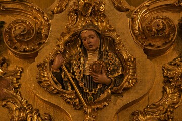 Brilliantly gilded colorful relief wood carving of St Scholastica with ethereal facial expression, holding crozier and sacred heart, at St Benedict Chapel, Jaen Cathedral, Spain