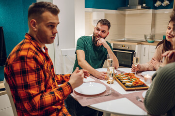 Group of friends enjoying dinner while sitting at the kitchen table together