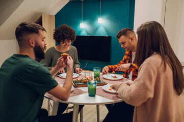 Group of friends enjoying dinner while sitting at the kitchen table together