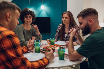 Group of friends enjoying dinner while sitting at the kitchen table together