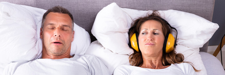 Woman Covering Her Ears With Headphones While Man Snoring