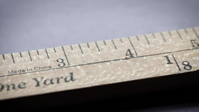 An yardstick with scales in yards and inches sliding in front of the camera