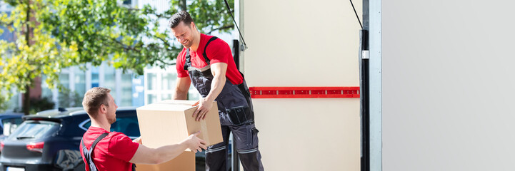 Two Young Male Movers Carrying Cardboard Boxes From Truck