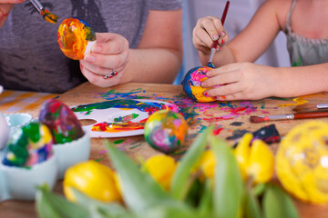 Decoration of colorful easter eggs for spring season. Hands of mum and daughter paint eggs for holiday. Fun, craft and decorate symbol of easter. Close up.