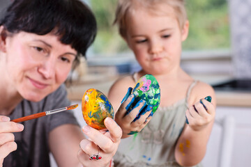 Fototapeta premium Decorate and paint easter eggs. Mum and daugter make handmade decoration and craft for spring holiday. Colorful egg and people. Closeup.