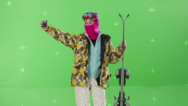 A young girl snowboarder taking a selfie against a green screen background in the studio. Active lifestyle in the mountains. Chroma key, tracking points