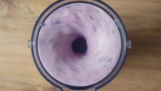 Running blender mixing raw blueberries and fresh milk, making a healthy delicious shake, top down view.