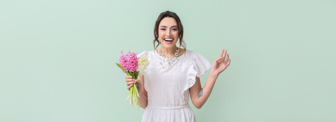 Beautiful happy young woman with bouquet of flowers on light green background with space for text. Hello spring
