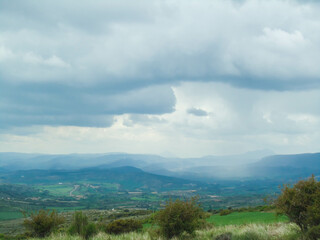 Landscape of green plains with a cloudy sky over distant mountains
