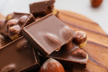 Pieces of tasty chocolate with hazelnuts on board, closeup