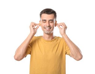 Smiling young man in yellow t-shirt putting earplugs on white background