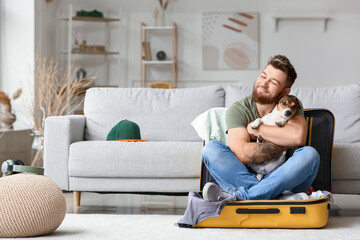 Young man with cute dog sitting in suitcase at home