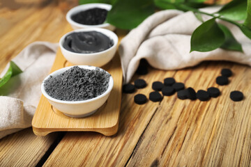 Bowls with ingredients for activated carbon facial mask on wooden background, closeup