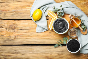 Composition with bowl of activated carbon facial mask, ingredients and eucalyptus branches on wooden background