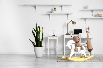 Interior of stylish child's room with modern workplace, houseplant and toy bear sitting on rocking...