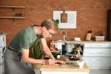Handsome young man making notes from cooking video tutorial in kitchen