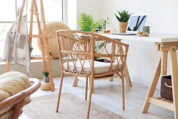 Modern workplace with laptop and wicker chair near light wall