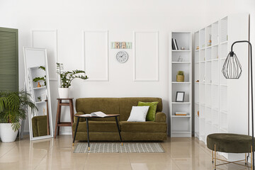 Interior of room with comfortable sofa, mirror and shelf unit near light wall