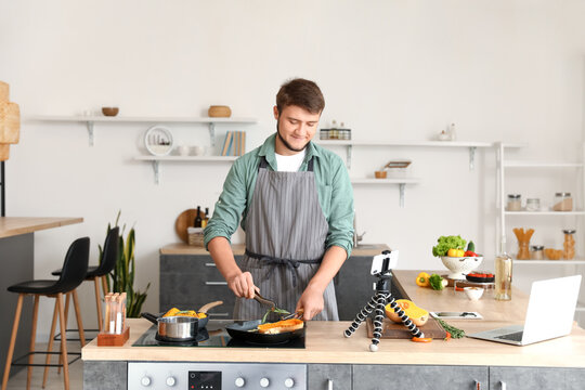 Young man cooking vegetables from video tutorial in kitchen