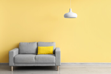 Comfortable sofa and modern lamp hanging near yellow wall