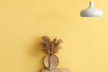 Vase with pampas grass on table and lamp hanging near yellow wall