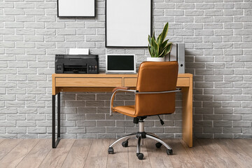 Comfortable workplace with modern laptop and printer near grey brick wall