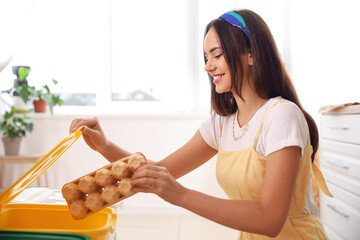 Young woman putting carton egg pack into bin in kitchen