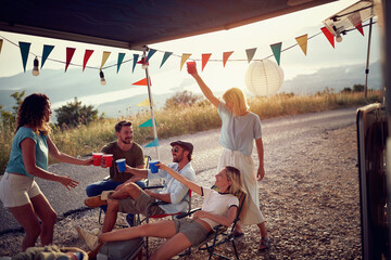 Group of friends in front of camper rv cheering with drinks. Fun, togetherness, lifestyle, nature concept..