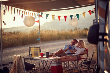 Couple sitting  in front of camper van and drinking .Travel and friendship celebration concept