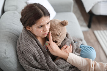 Mother applying remedy on skin of her little daughter ill with chickenpox at home