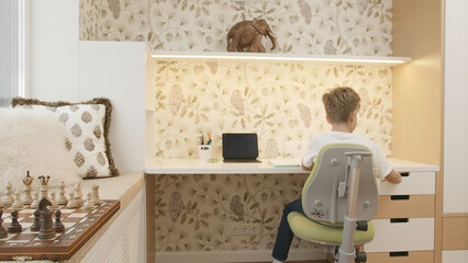 Interior of children's room with boy sitting at table. Creative. Boy is studying at desk. Children's room of smart boy studying at table