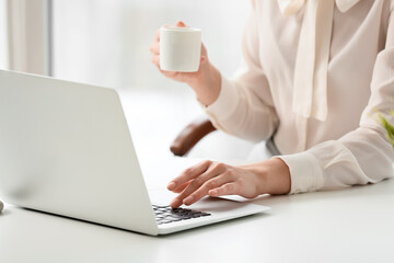 Young secretary drinking coffee while working on laptop in office, closeup