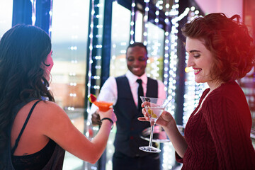 The fun has just begun. Shot of a waiter serving two women cocktails at a party.