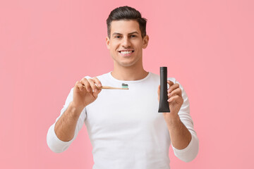 Handsome young man with activated charcoal tooth paste and brush on pink background