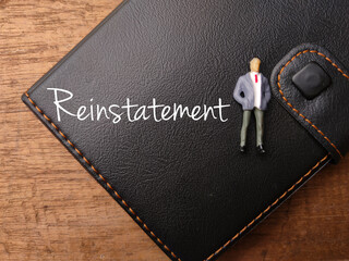 Notebook and miniature people with text Reinstatement on a wooden background.