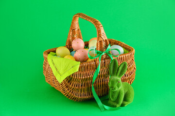 Wicker basket of painted Easter eggs and toy bunny on green background