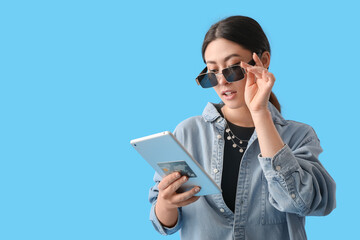 Young woman with tablet computer and credit card on color background. Shopping online