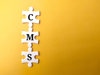Top view white puzzle with text CMS on a yellow background.